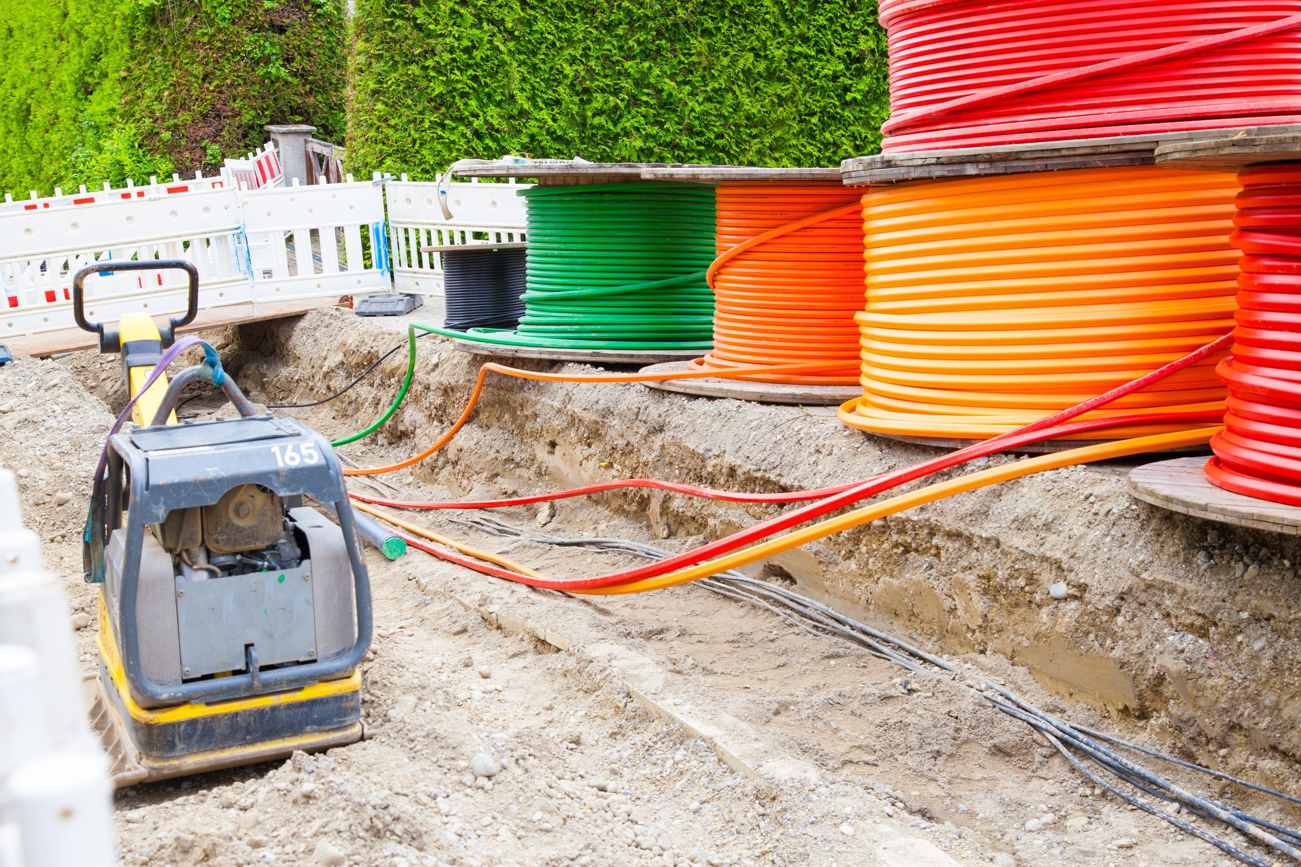 Baustelle mit offenem Graben, Rüttelplatte und Kabeltrommeln mit Leerrohren